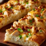Close-up of sliced homemade Costco chicken bake with golden brown dough, melted mozzarella and cheddar cheese, diced chicken, crispy bacon pieces, and chopped green onions on a white rectangular plate