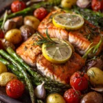 Close-up of one-pan lemon herb baked salmon fillets with roasted baby potatoes, asparagus spears, cherry tomatoes, garnished with lemon slices and fresh rosemary and thyme on a rustic plate under warm natural light
