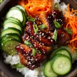 Close-up of a vibrant gochujang chicken bowl with tender chicken thighs glazed in a sticky red sauce, white rice, julienned carrots, sliced cucumbers, chopped scallions, and toasted sesame seeds on a rustic surface with warm lighting