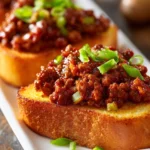 Close-up of open-faced Texas Toast Sloppy Joes with ground beef, green bell pepper, onions, and glossy rich red tomato sauce on golden toasted bread, served on a white rectangular plate.