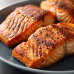 Close-up of air fryer salmon fillets with a golden crust on a clean white plate.