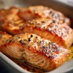 Close-up of baked creamy salmon with a golden crust and herbs on a white plate