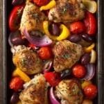 Close-up of a sheet pan with Mediterranean chicken, colorful vegetables, and herbs.